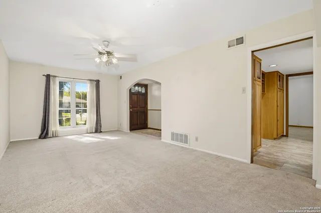 an empty room with chandelier fan and windows