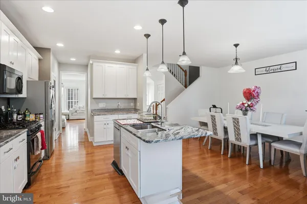 a kitchen with stainless steel appliances kitchen island granite countertop a stove a sink a refrigerator and a dining table with wooden floor