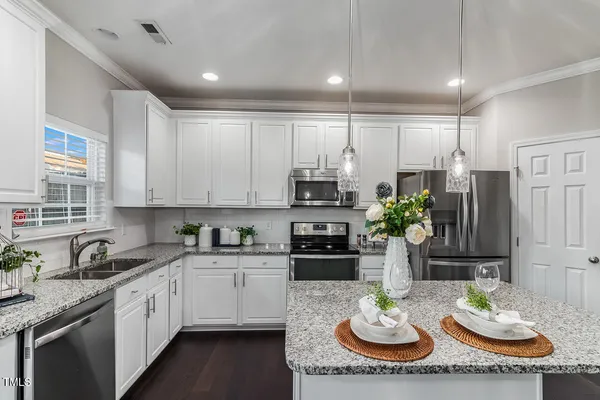 a kitchen with stainless steel appliances kitchen island granite countertop a sink a stove a dining table and chairs with wooden floor