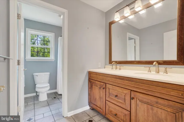 a spacious bathroom with a toilet a double vanity sink and a mirror