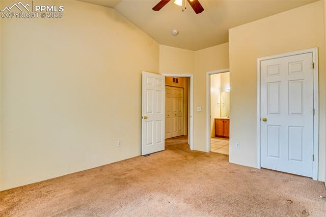 2049 Legacy Ridge View, Unit 111 Colorado Springs, CO 80910 - Photo 27 of 32 Unfurnished bedroom with light colored carpet, vaulted ceiling, connected bathroom, and a ceiling fan