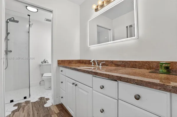 a bathroom with a granite countertop sink a mirror and shower