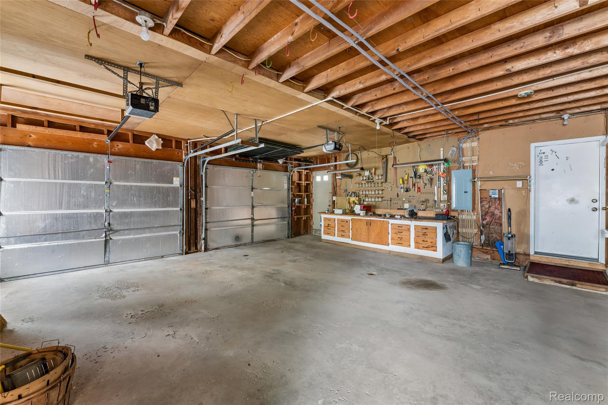 422 East Road Holly, MI 48442 - Photo 39 of 51 Spacious garage featuring two overhead doors with automatic openers, exposed wood beam ceiling, concrete flooring, and a built-in workbench with storage