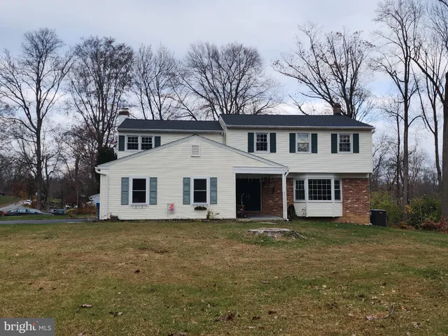 a view of a white house next to a yard with large trees