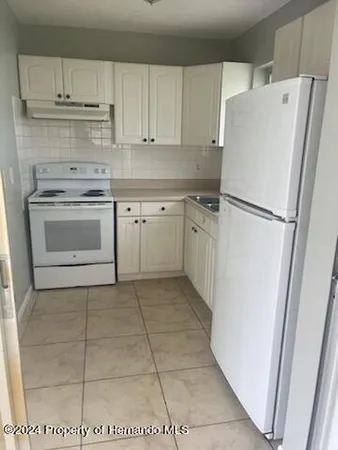 a white refrigerator freezer and a stove sitting inside of a kitchen with granite countertop white cabinets