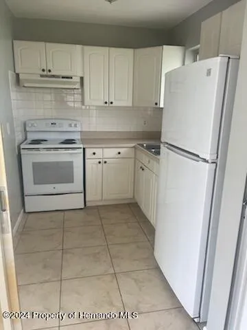 a white refrigerator freezer and a stove sitting inside of a kitchen with granite countertop white cabinets