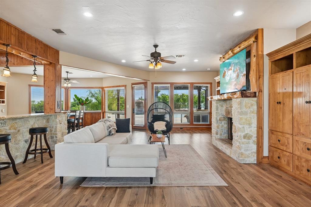 2085 Switzer Road Sanger, TX 76266 - Photo 6 of 39 Spacious living area featuring wood-finish flooring, a stone fireplace with a wood mantel, a built-in entertainment center with natural wood cabinetry, and extensive windows with exterior views