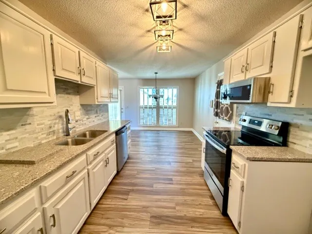 a large kitchen with stainless steel appliances granite countertop a stove a sink dishwasher and a microwave oven with white cabinets