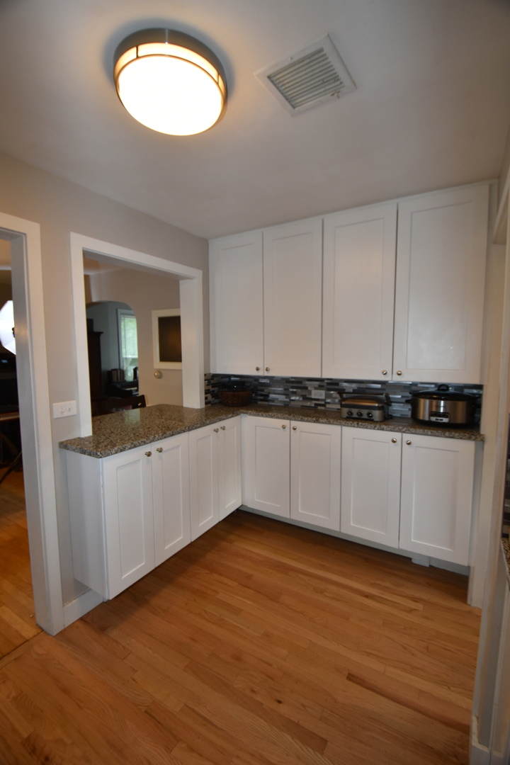 25W756 Jewell Road Wheaton, IL 60187 - Photo 3 of 25 a large white kitchen with granite countertop a stove a sink and white cabinets with wooden floor