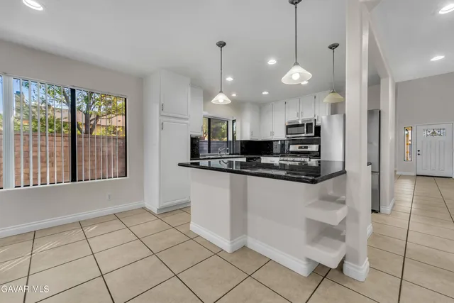 a kitchen with stainless steel appliances kitchen island granite countertop a refrigerator a stove a sink and a microwave oven with white cabinets