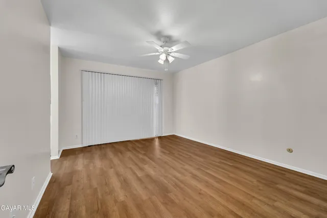 a view of an empty room with wooden floor and a ceiling fan