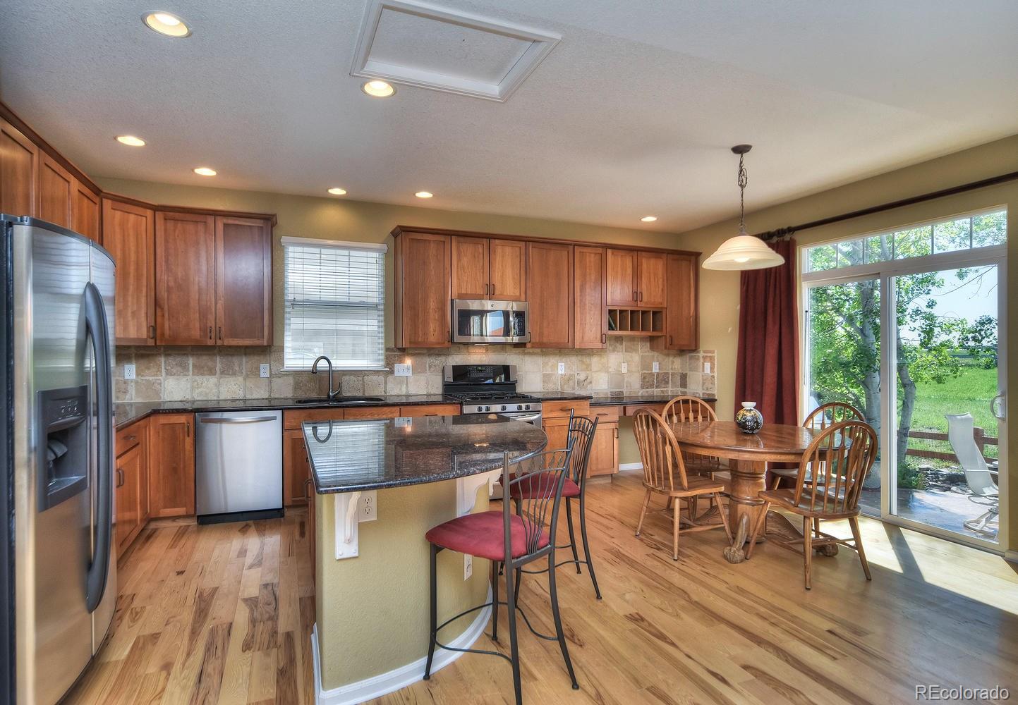 4464 Eagle River Run Broomfield, CO 80023 - Photo 10 of 32 a kitchen with stainless steel appliances granite countertop wooden cabinets a stove top oven a granite counter tops and a view of living room