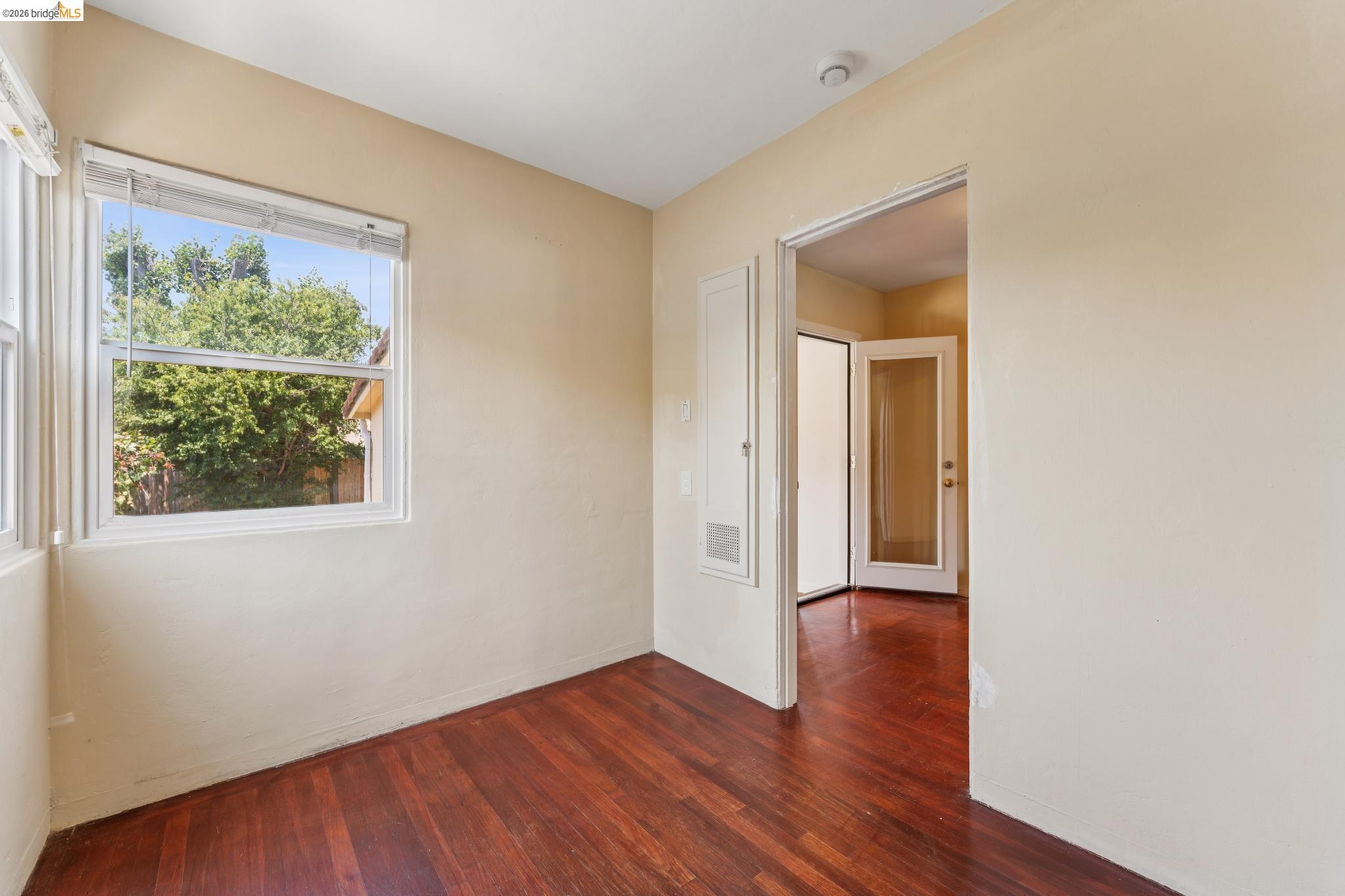 2879 Rheem Avenue Richmond, CA 94804 - Photo 18 of 45 Hardwood-finish flooring throughout, featuring a white-trimmed window, neutral wall tones, and a doorway leading to a room with a French door