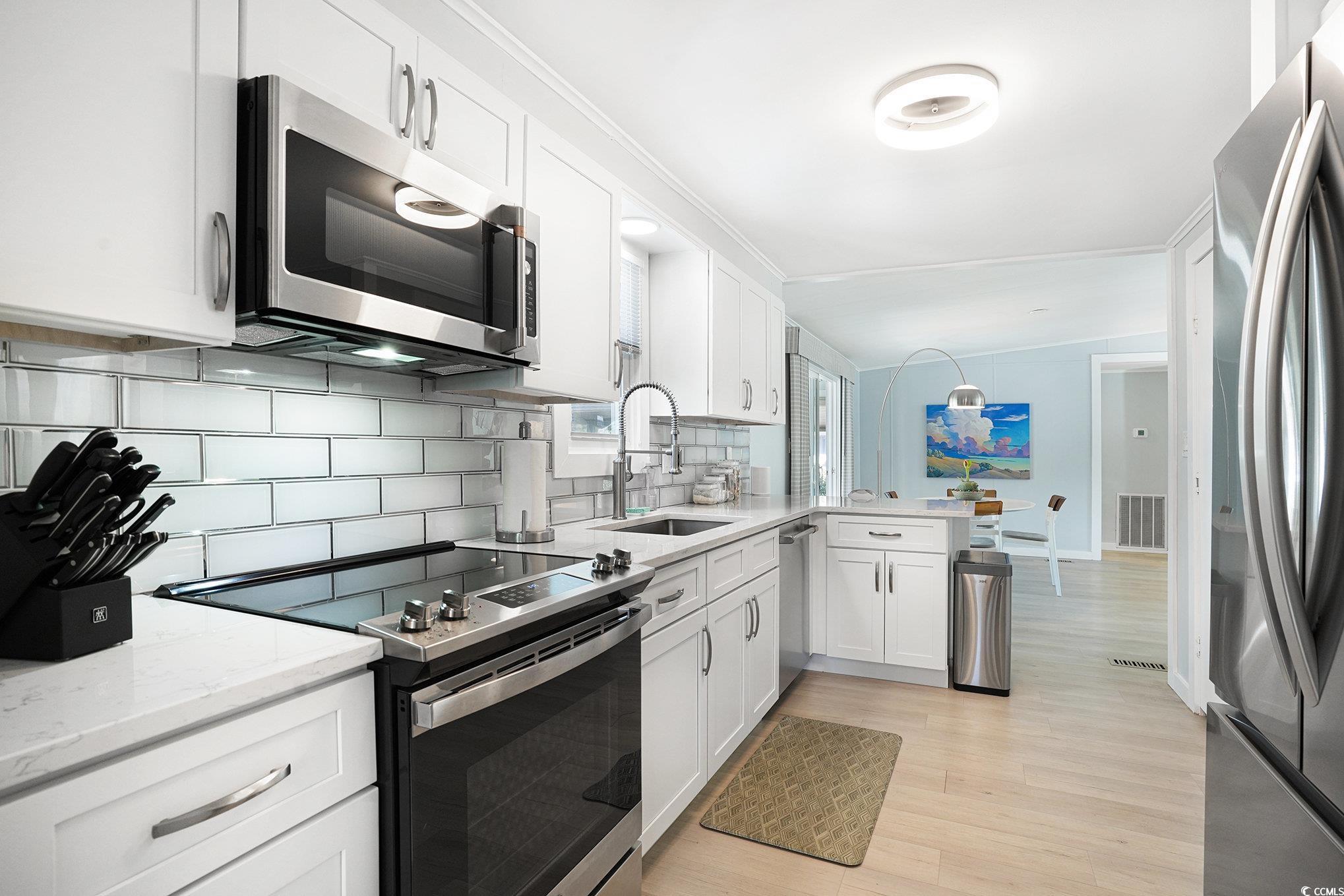 3268 Pecan Trail Murrells Inlet, SC 29576 - Photo 13 of 38 Kitchen with stainless steel appliances, white cabinetry, light stone counters, light wood-style floors, and backsplash