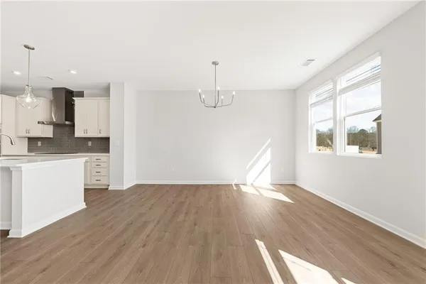a view of empty room with wooden floor and kitchen view