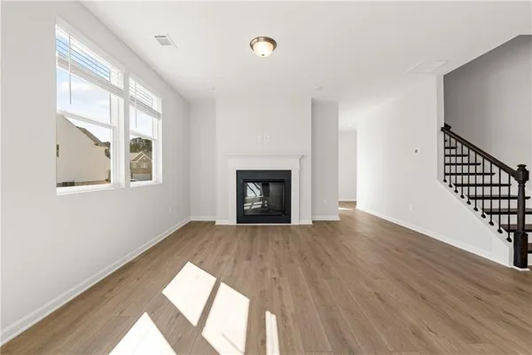 a view of an empty room with wooden floor fireplace and a window