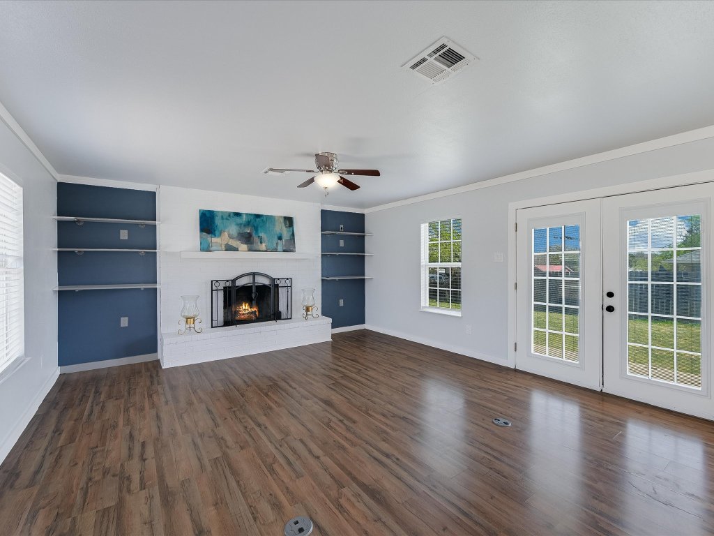 155 Travis Lane Spicewood, TX 78669 - Photo 1 of 33 an empty room with wooden floor fireplace and windows