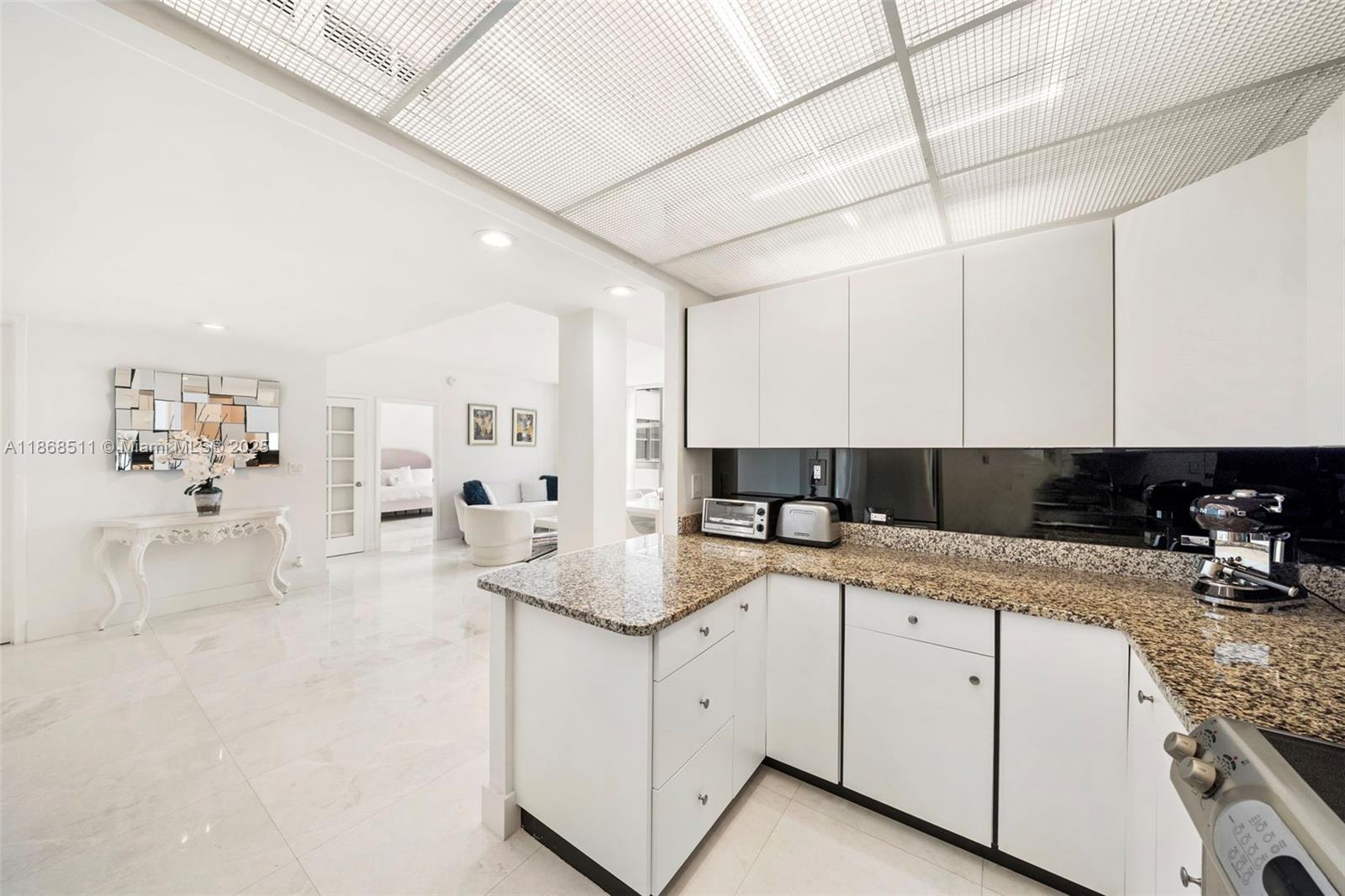 5055 Collins Avenue, Unit 10G Miami Beach, FL 33140 - Photo 4 of 20 a kitchen with a sink dishwasher and white cabinets with wooden floor