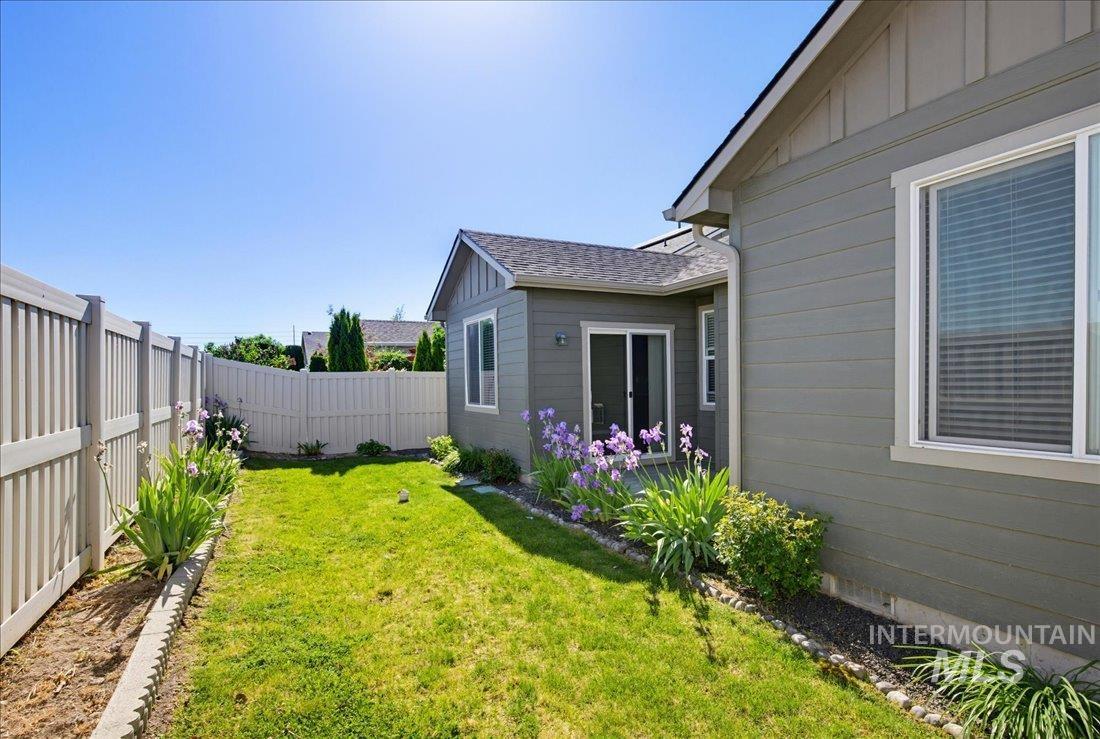 12460 West Azure Street Boise, ID 83713 - Photo 32 of 34 Fenced backyard featuring a manicured lawn, landscaping with purple flowering plants, and a gravel bed border