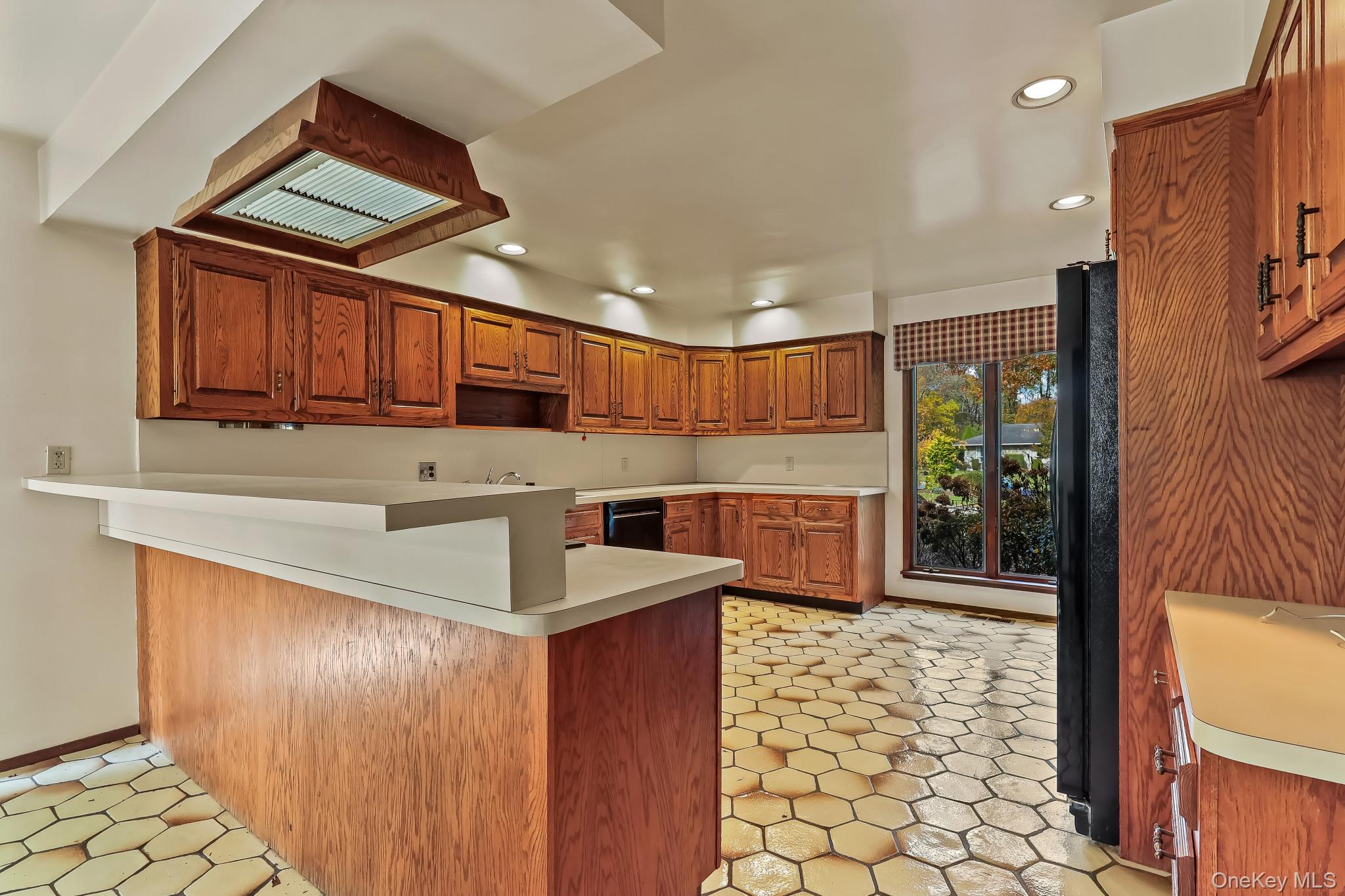 37 Century Trail Harrison, NY 10528 - Photo 14 of 43 Kitchen featuring brown cabinetry, a peninsula, recessed lighting, light countertops, and black appliances