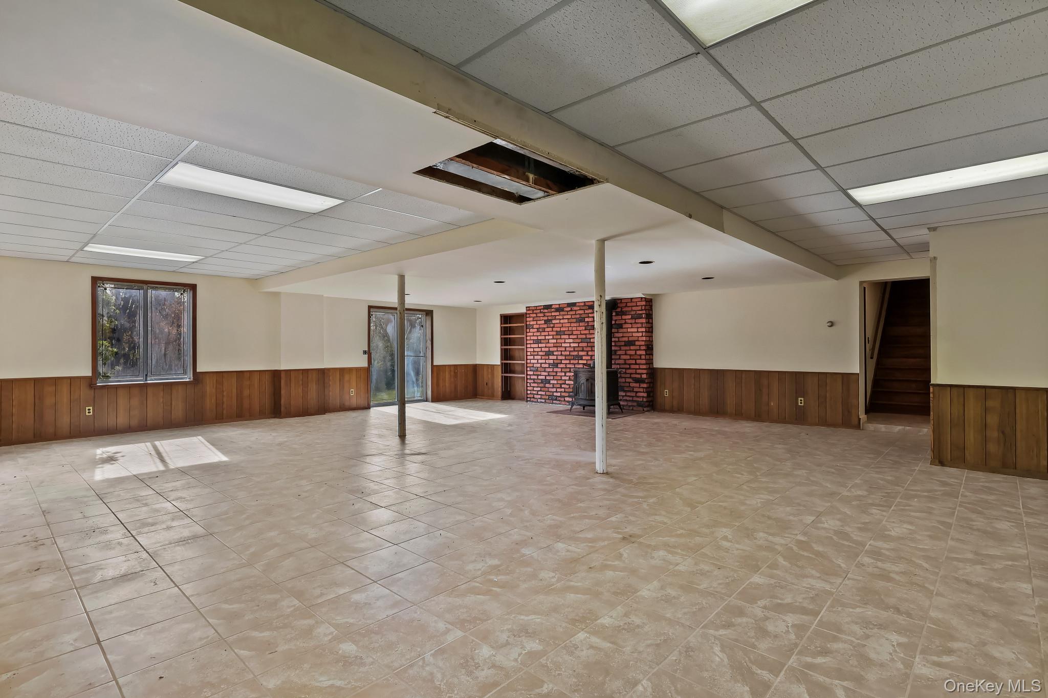 37 Century Trail Harrison, NY 10528 - Photo 34 of 43 Walkout finished basement with a drop ceiling, a wainscoted wooden walls, stairs, and light tile patterned floors, wood burning stove