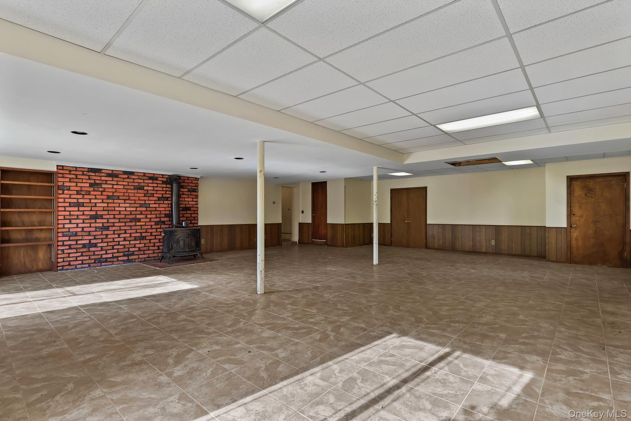 37 Century Trail Harrison, NY 10528 - Photo 36 of 43 Finished basement with a paneled ceiling, a wood stove, wainscoting, and wooden walls