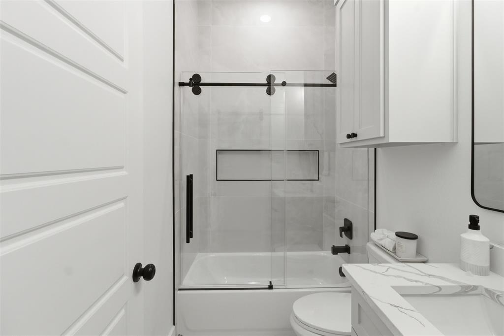 435 Waterboard Road Trinidad, TX 75163 - Photo 20 of 39 Modern bathroom featuring a white panel door, sliding glass shower enclosure with matte black hardware, white subway tile shower surround with recessed niche, and a white vanity with integrated sink and stone-finish countertop