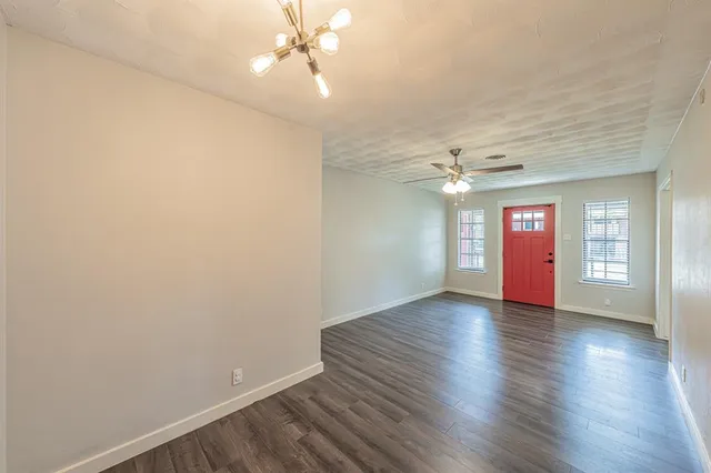 an empty room with wooden floor fan and windows
