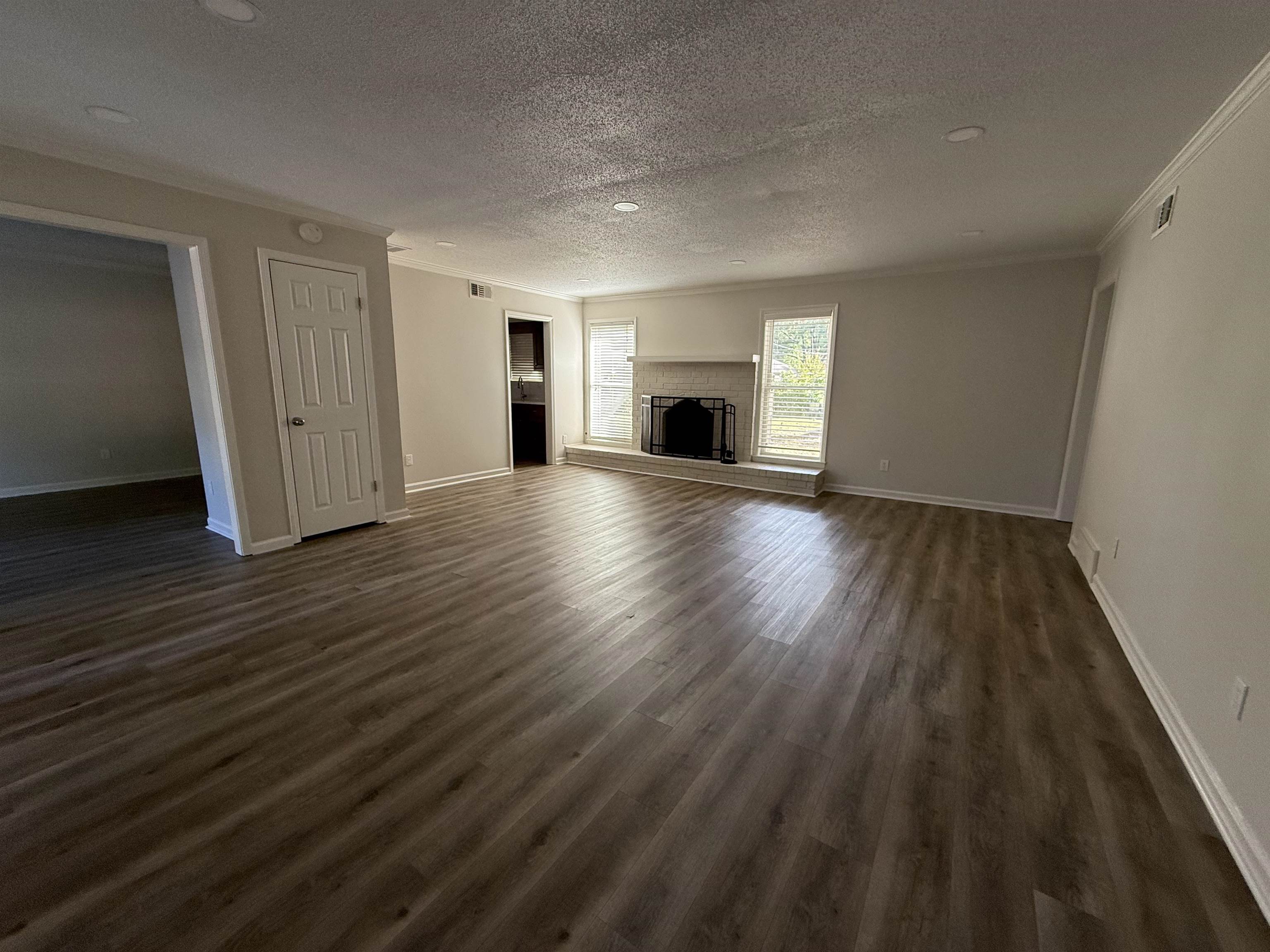 5701 Baird Drive Memphis, TN 38119 - Photo 2 of 12 Unfurnished living room with a textured ceiling, crown molding, dark wood-style floors, and a fireplace with raised hearth
