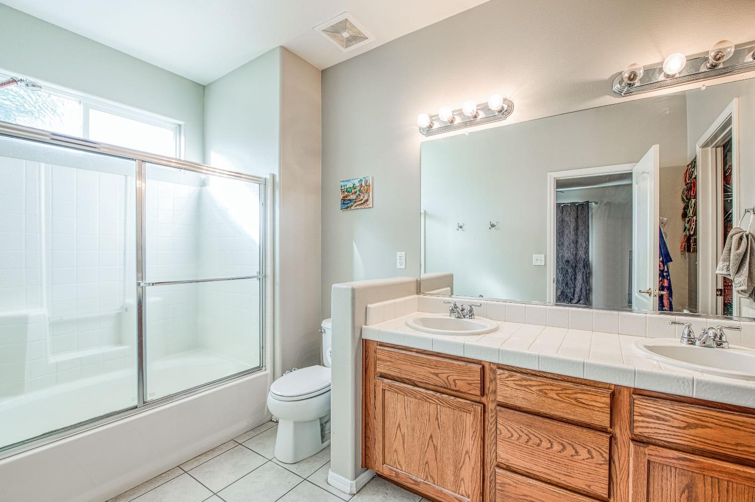 1648 North Avignon Lane Clovis, CA 93619 - Photo 22 of 27 a bathroom with a granite countertop sink toilet a large mirror a vanity and shower