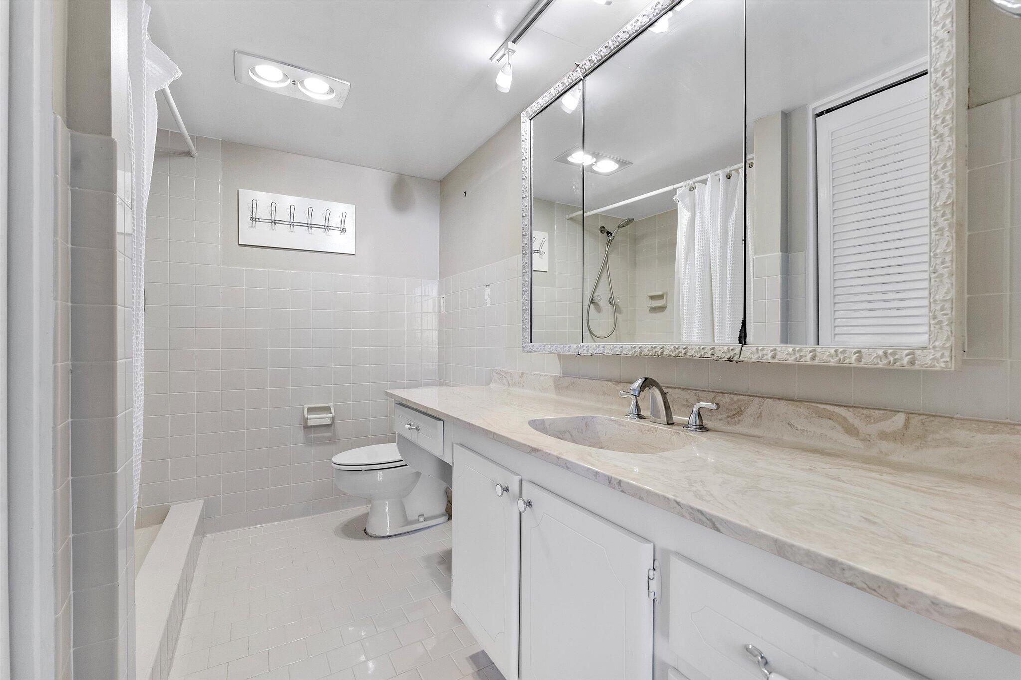 501 Southwest 11th Place, Unit 418 Boca Raton, FL 33432 - Photo 15 of 35 a bathroom with a granite countertop sink a toilet and a mirror