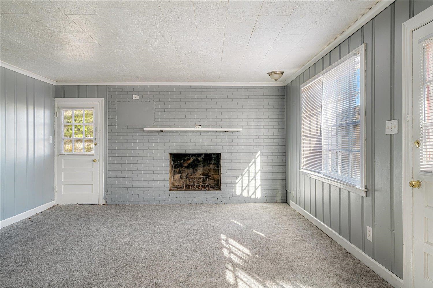 1114 Brownlee Road Memphis, TN 38116 - Photo 15 of 32 Unfurnished living room with a brick fireplace, wooden walls, carpet flooring, and ornamental molding