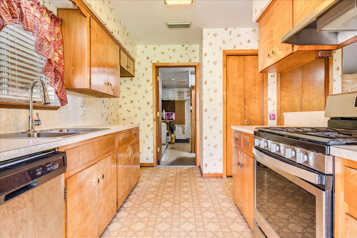 6626 Isabelle Drive Austin, TX 78752 - Photo 14 of 27 Galley kitchen featuring light wood cabinetry, a stainless steel range with overhead ventilation, a stainless steel double basin sink with a gooseneck faucet, an integrated dishwasher, and patterned flooring