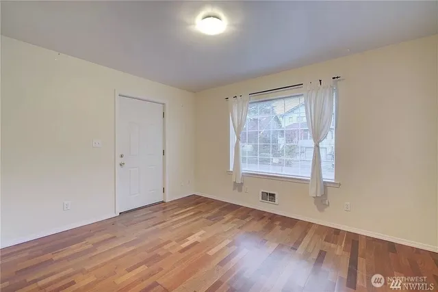 a view of an empty room with a window and wooden floor