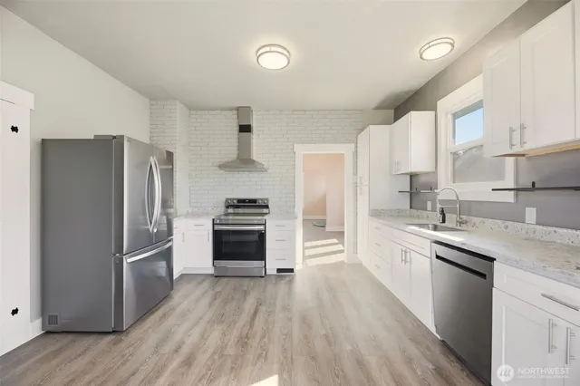 a kitchen with granite countertop a refrigerator a sink dishwasher and a stove top oven with wooden floor