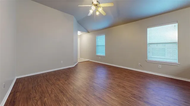 an empty room with wooden floor chandelier fan and windows