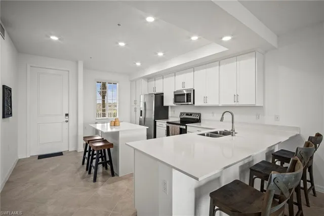 a kitchen with stainless steel appliances kitchen island granite countertop a table chairs sink and white cabinets