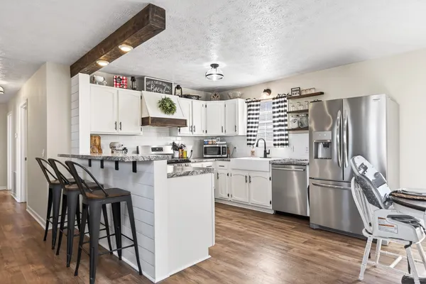 a kitchen with granite countertop a refrigerator a stove a sink and white cabinets with wooden floor