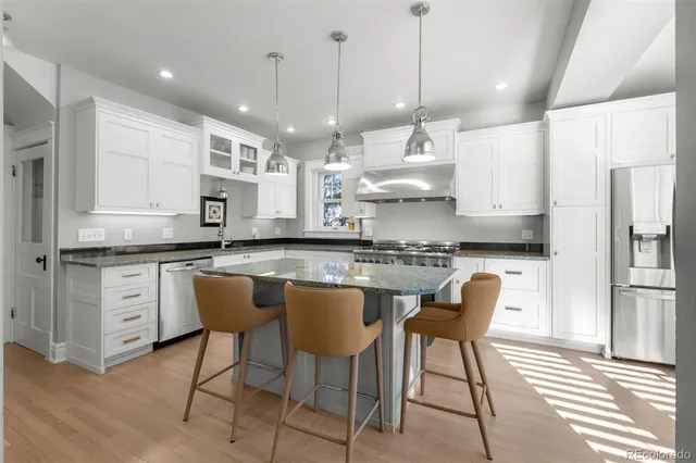 a kitchen with stainless steel appliances granite countertop a sink a stove a refrigerator and white cabinets with wooden floor