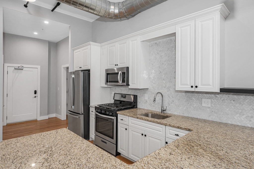 491 Dutton Street, Unit 320 Lowell, MA 01854 - Photo 7 of 31 a kitchen with stainless steel appliances granite countertop a refrigerator sink and stove