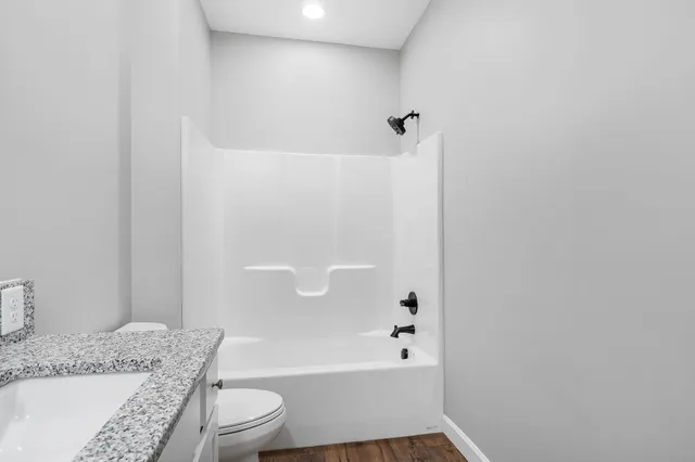 a bathroom with a granite countertop bathtub shower sink vanity and toilet