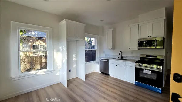 a kitchen with stainless steel appliances granite countertop a stove top oven a sink dishwasher a refrigerator and a microwave oven with wooden floor