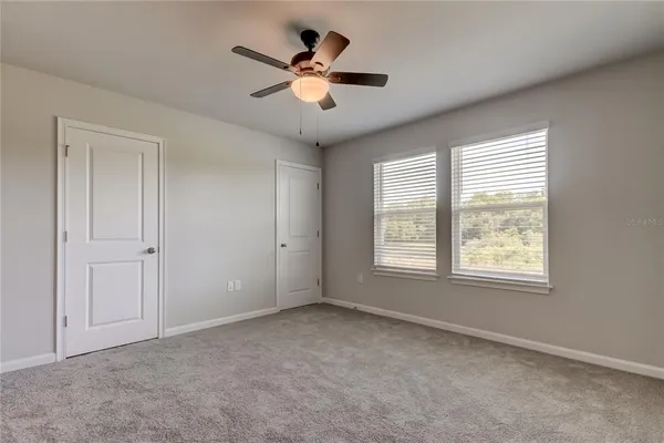an empty room with chandelier fan and windows