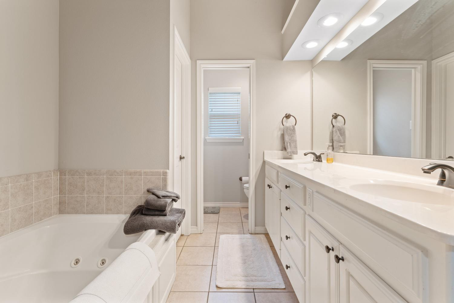 5614 100th Street Lubbock, TX 79424 - Photo 17 of 27 a spacious bathroom with double vanity a mirror and a bathtub