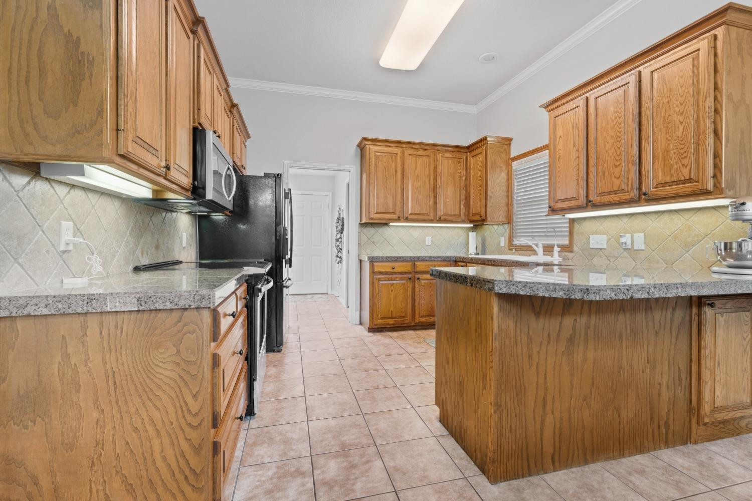 5614 100th Street Lubbock, TX 79424 - Photo 9 of 27 a kitchen with kitchen island granite countertop a sink stainless steel appliances and cabinets