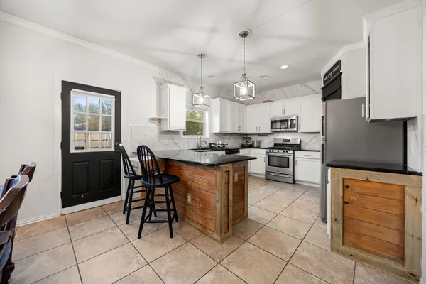 a kitchen with stainless steel appliances granite countertop a stove a sink a refrigerator and a dining table with wooden cabinets