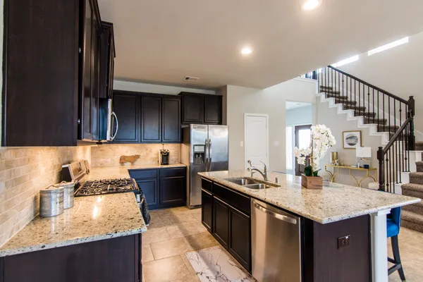a kitchen with stainless steel appliances granite countertop a stove top oven a sink dishwasher a dining table and chairs with wooden floor