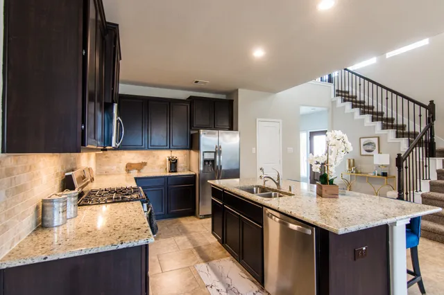 a kitchen with stainless steel appliances granite countertop a stove top oven a sink dishwasher a dining table and chairs with wooden floor