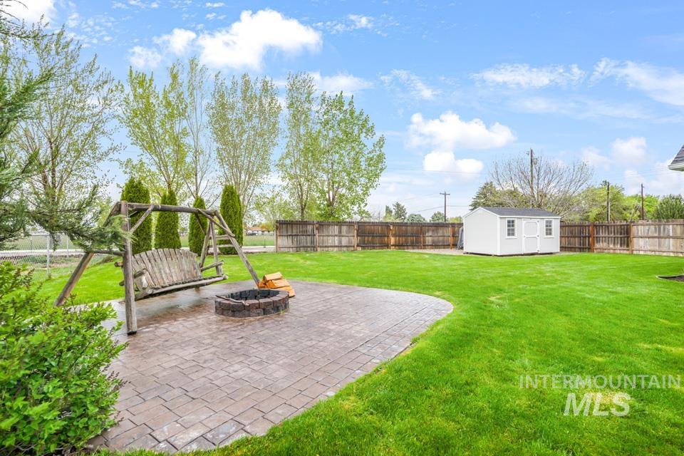 8271 Washoe Road Fruitland, ID 83619 - Photo 9 of 29 Expansive backyard featuring a paver patio with a built-in fire pit, a wooden swing, a manicured lawn, and a white storage shed