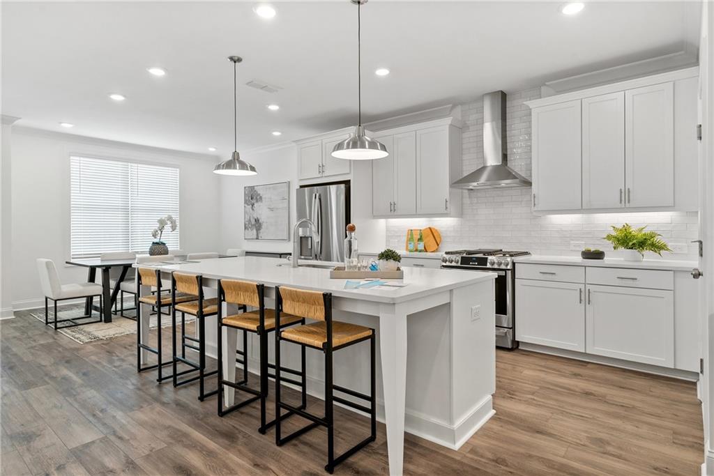 a kitchen with stainless steel appliances granite countertop a stove a sink a kitchen island and chairs with wooden floor